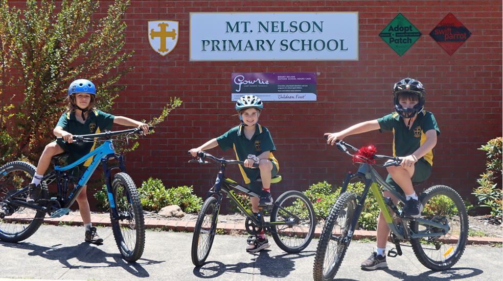 three students on their bicycles in front of Mount Nelson Primary School.