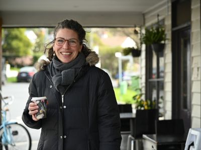 Woman in black winter coat smiling and holding a coffee outside a West Hobart cafe.